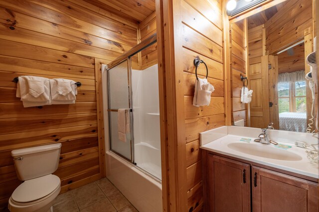 full bathroom featuring bath / shower combo with glass door, vanity, tile patterned flooring, toilet, and wood walls