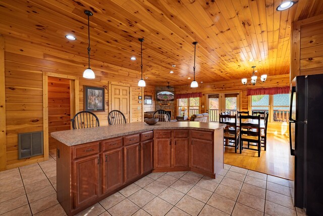 kitchen featuring black fridge, pendant lighting, light tile patterned floors, a kitchen island, and a stone fireplace