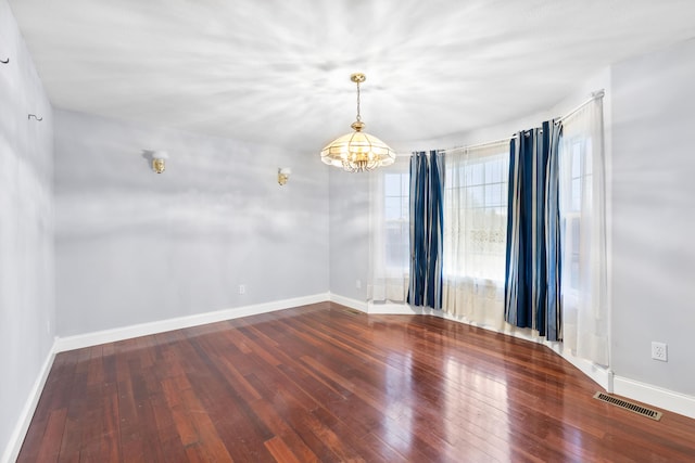 spare room with hardwood / wood-style flooring, baseboards, visible vents, and a chandelier