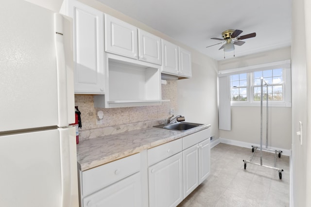 kitchen featuring tasteful backsplash, white cabinets, freestanding refrigerator, light countertops, and a sink