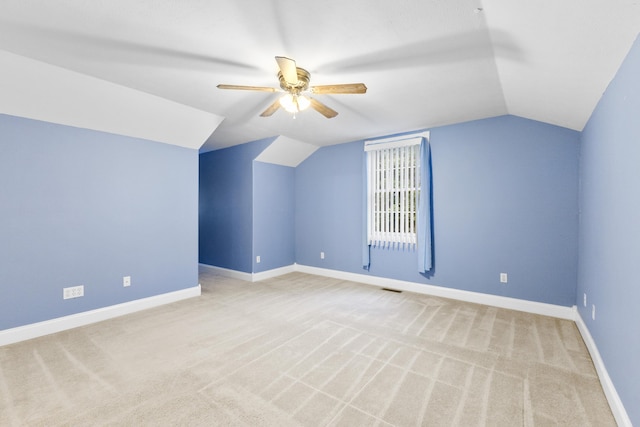 additional living space with light colored carpet, visible vents, a ceiling fan, vaulted ceiling, and baseboards