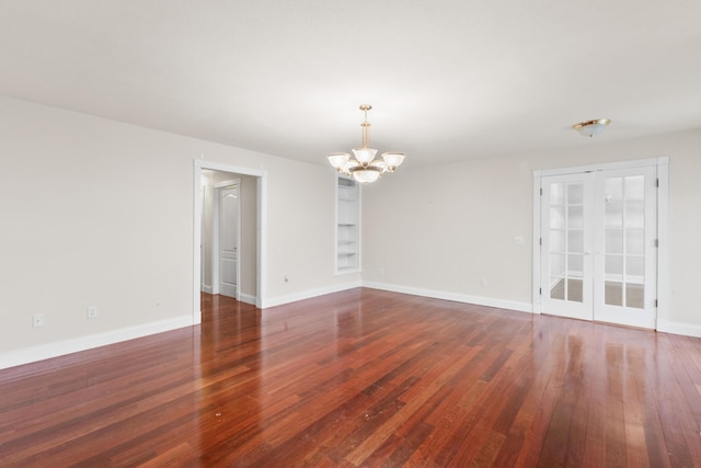 spare room with a chandelier, wood-type flooring, and baseboards