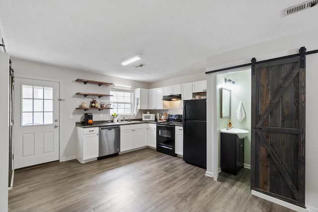 kitchen featuring black appliances, a barn door, white cabinets, and sink