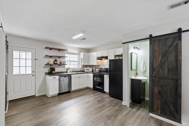 kitchen featuring black appliances, a barn door, white cabinets, and sink