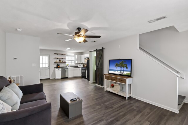 living room with a barn door, dark hardwood / wood-style floors, and ceiling fan