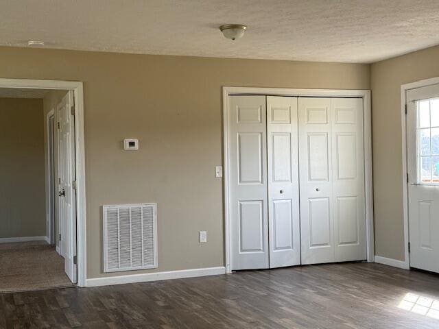 unfurnished bedroom featuring baseboards, visible vents, dark wood-style flooring, a closet, and a textured ceiling