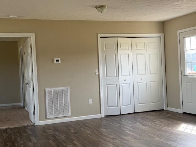 unfurnished bedroom featuring a closet, baseboards, visible vents, and dark wood-style flooring