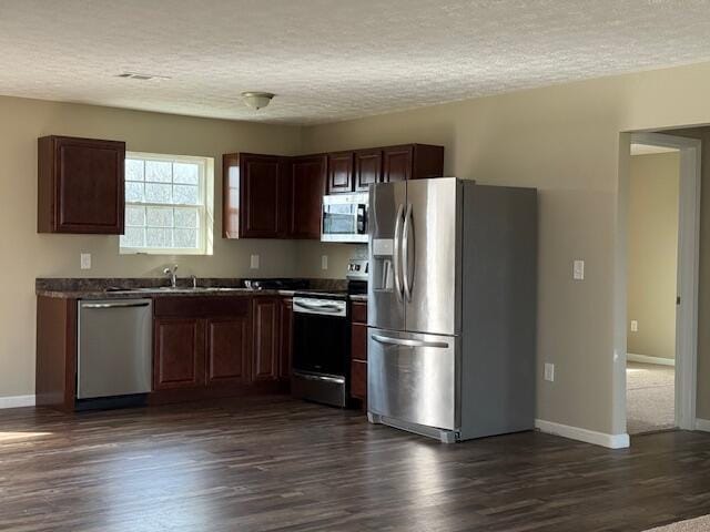 kitchen featuring stainless steel appliances, dark countertops, dark wood-style floors, and a textured ceiling