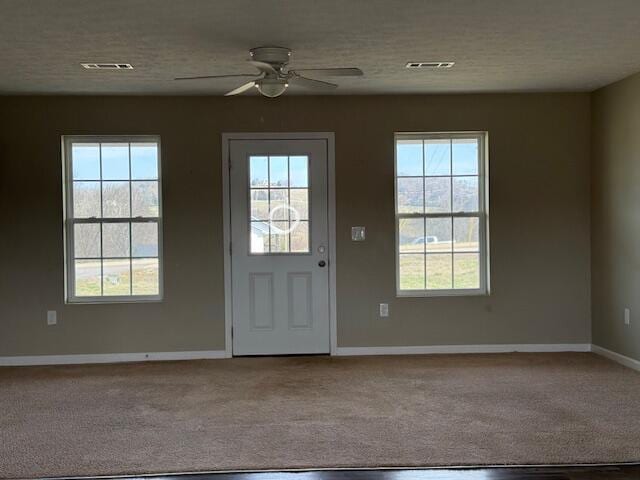 doorway featuring carpet flooring, a ceiling fan, visible vents, and a textured ceiling