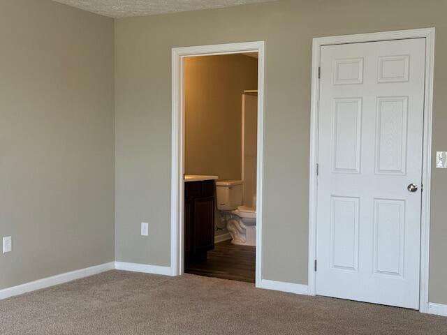 unfurnished bedroom with baseboards, carpet floors, and ensuite bathroom