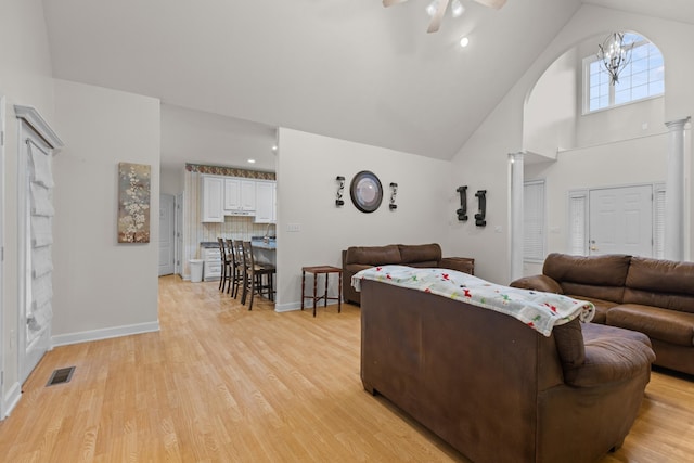 living room featuring ceiling fan with notable chandelier, high vaulted ceiling, light hardwood / wood-style flooring, and decorative columns