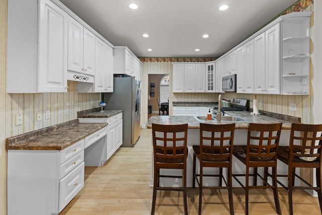 kitchen featuring white cabinets, a kitchen breakfast bar, light hardwood / wood-style floors, kitchen peninsula, and stainless steel appliances