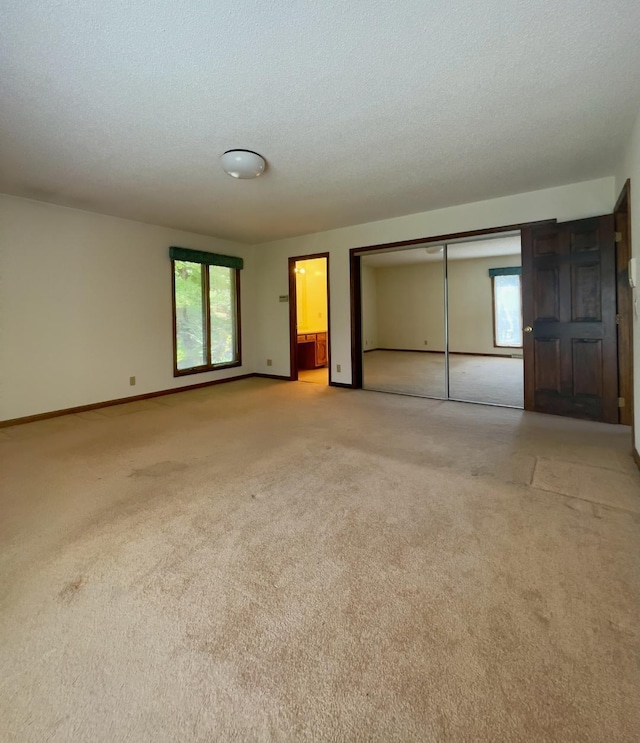 unfurnished bedroom featuring connected bathroom, a closet, light colored carpet, and a textured ceiling