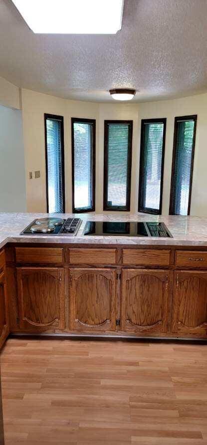 kitchen with a textured ceiling, light wood-type flooring, black electric stovetop, and stainless steel gas stovetop