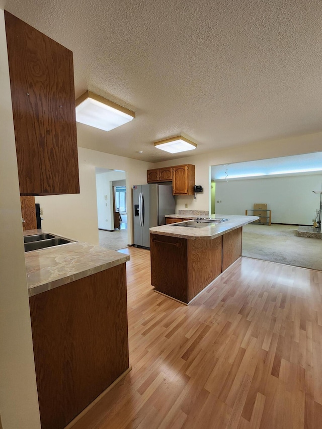 kitchen featuring stainless steel fridge, light wood-type flooring, kitchen peninsula, and a textured ceiling