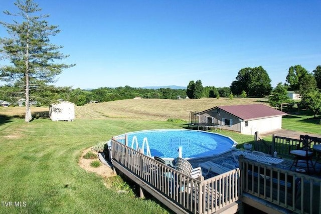 view of swimming pool with a rural view, a storage unit, and a lawn