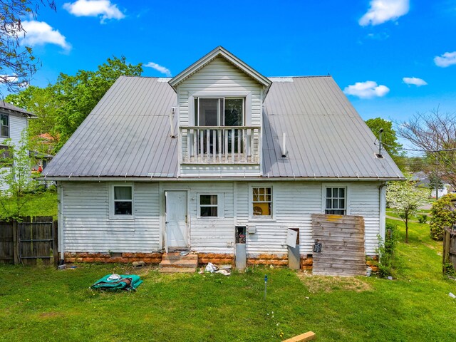 rear view of property featuring metal roof, a lawn, a balcony, and fence