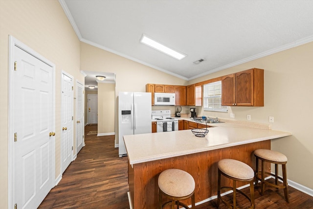 kitchen with lofted ceiling, a peninsula, white appliances, and dark wood finished floors