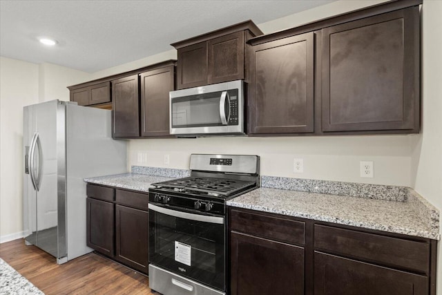 kitchen with light stone countertops, dark brown cabinets, wood-type flooring, and stainless steel appliances
