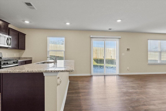 kitchen featuring sink, dark wood-type flooring, dark brown cabinets, stainless steel appliances, and an island with sink