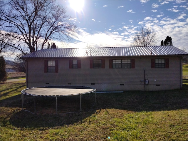 back of property with a trampoline and a yard