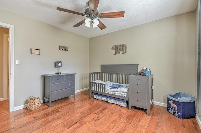 bedroom featuring ceiling fan, a nursery area, a textured ceiling, and light hardwood / wood-style flooring