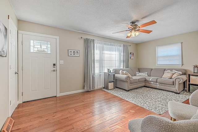 living room with ceiling fan, a textured ceiling, and light wood-type flooring