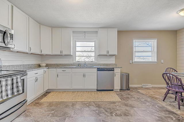 kitchen with stainless steel appliances, sink, white cabinets, and light stone counters