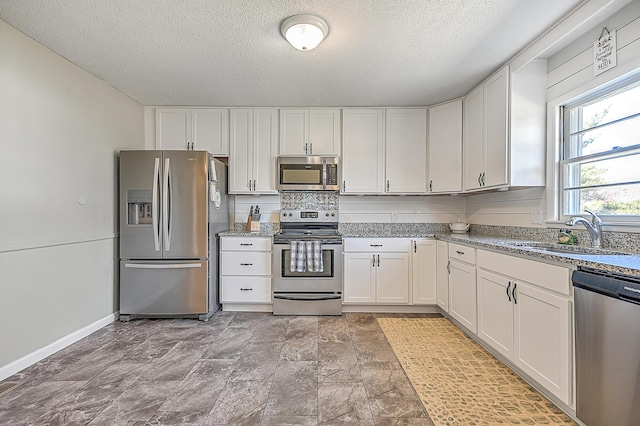 kitchen with sink, white cabinetry, a textured ceiling, appliances with stainless steel finishes, and light stone countertops