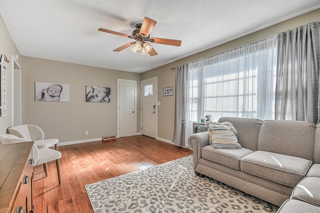 living room featuring ceiling fan, light hardwood / wood-style floors, and a textured ceiling