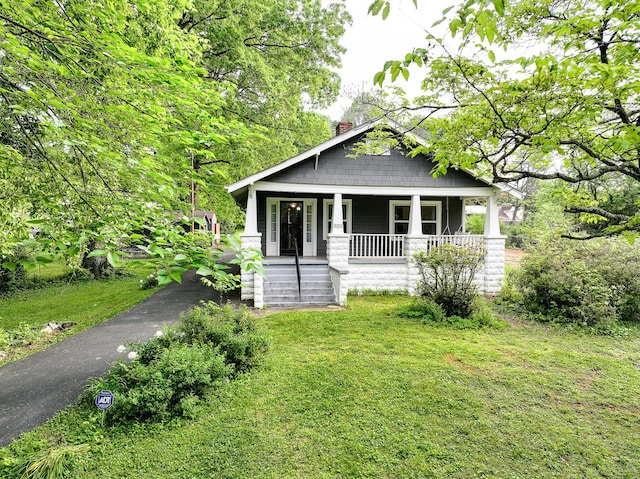 view of front of property featuring a chimney, a porch, and a front lawn