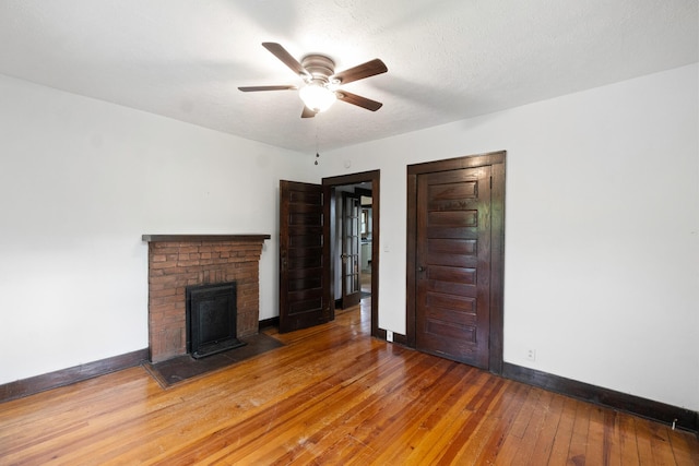 unfurnished living room with wood-type flooring, a ceiling fan, baseboards, and a brick fireplace