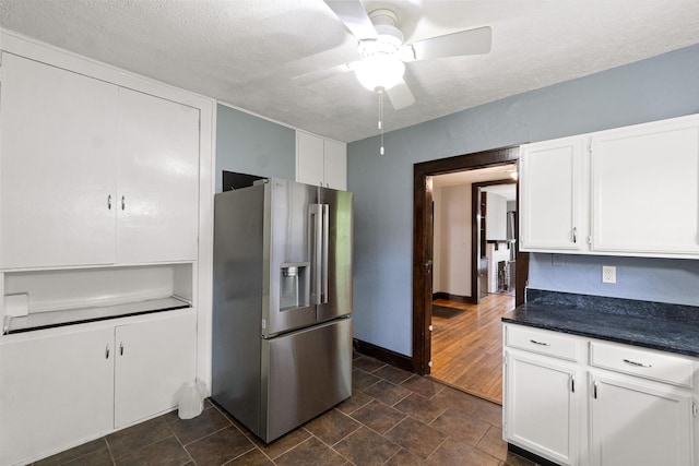 kitchen featuring a ceiling fan, dark countertops, baseboards, white cabinets, and stainless steel fridge