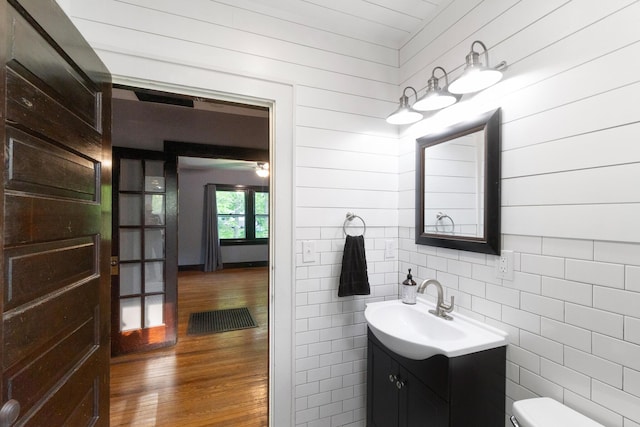 half bath with toilet, wood walls, wood finished floors, and vanity