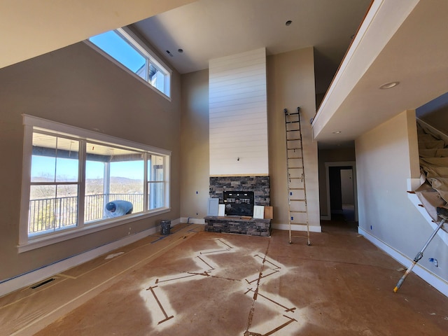 unfurnished living room featuring visible vents, a fireplace, a towering ceiling, and baseboards
