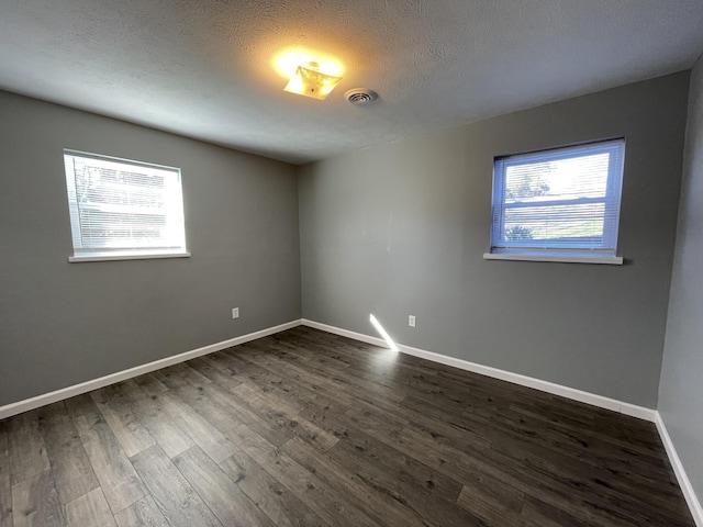 empty room with a healthy amount of sunlight, dark hardwood / wood-style flooring, and a textured ceiling