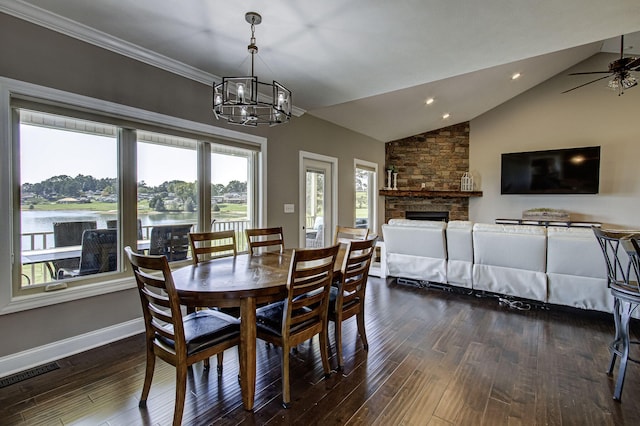 dining area with lofted ceiling, ceiling fan with notable chandelier, a stone fireplace, a water view, and dark hardwood / wood-style floors