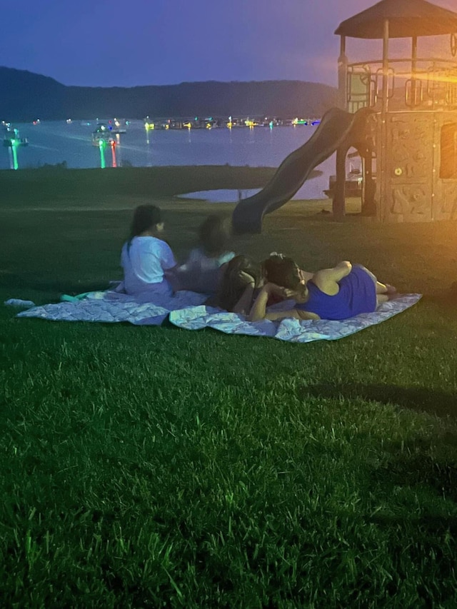 yard at dusk featuring a playground and a water view