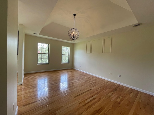 spare room with a chandelier, a raised ceiling, and light hardwood / wood-style flooring