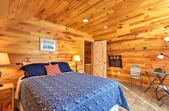 bedroom with lofted ceiling, wooden walls, light tile patterned floors, and wooden ceiling