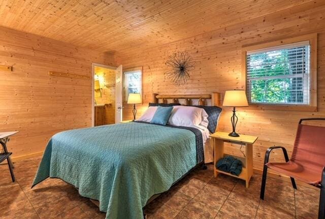 bedroom with dark tile patterned flooring, wood ceiling, and wooden walls