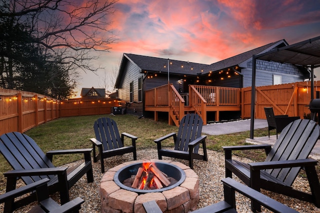 patio terrace at dusk featuring a fire pit, a lawn, and a deck