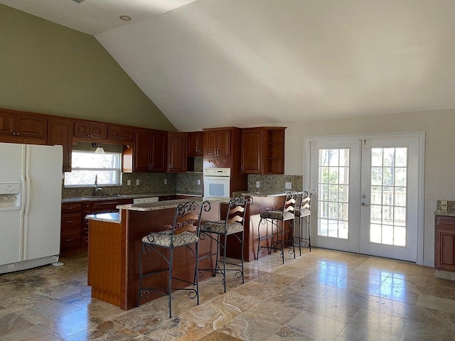 kitchen with white appliances, french doors, backsplash, and a breakfast bar area