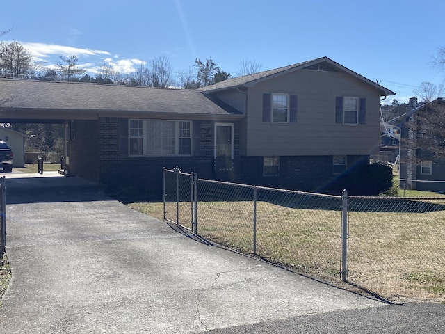 tri-level home with a fenced front yard, brick siding, an attached carport, driveway, and a front lawn