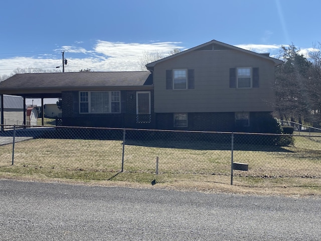 split level home featuring brick siding, a fenced front yard, an attached carport, and a front yard