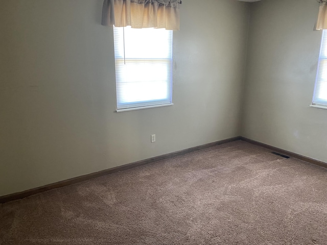 carpeted empty room with a healthy amount of sunlight, visible vents, and baseboards