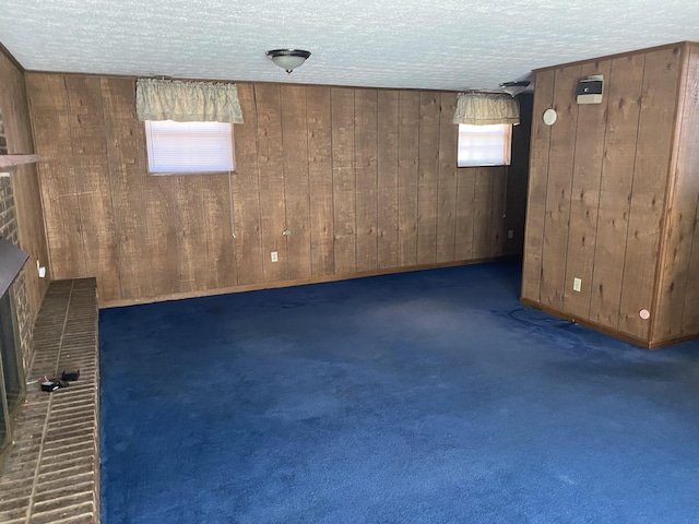 basement with a textured ceiling, wood walls, a fireplace, and carpet flooring