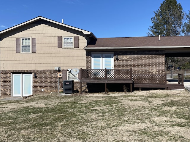 back of house featuring cooling unit, brick siding, a shingled roof, a lawn, and a wooden deck