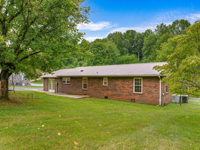 back of property featuring crawl space, brick siding, a lawn, and metal roof