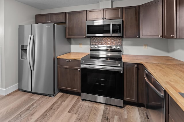 kitchen with stainless steel appliances, dark brown cabinets, light wood-type flooring, and wood counters